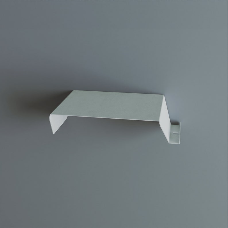 A minimalist, white metal shelf with a clean, modern design. The shelf has a flat top and a downward-sloping front edge, with a small, rectangular support bracket. The shelf is mounted on a gray wall.