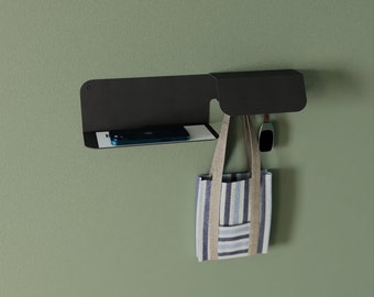 May include: A black metal wall shelf with a small, rectangular shelf and a hook. A blue and white striped tote bag hangs from the hook. A black phone and a black watch are on the shelf.