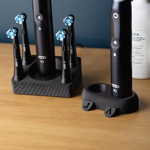 May include: Black electric toothbrush and brush heads with blue bristles in a black holder. The toothbrush has the brand name "Oral B" and the number "IO" printed on it. A second toothbrush is in a smaller holder with the initials "J A".
