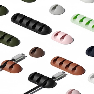 May include: A selection of cable tidies in diverse colours, such as black, brown, green, pink, and white. Some tidies are holding black cables with silver connectors. The tidies have multiple slots for holding cables and wires.