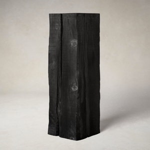 Puede incluir: Un pedestal de madera negro con una superficie rugosa y texturizada. El pedestal está hecho de varias piezas de madera que se han unido.