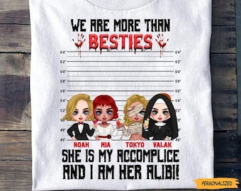 May include: White t-shirt with a black and white illustration of four women with red, black, and white hair. The women are standing in front of a white wall with black lines and numbers. The text "We are more than besties" is above the women, and the text "She is my accomplice and I am her alibi!" is below the women.