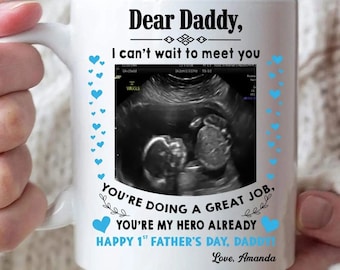 May include: White ceramic mug with the text "Dear Daddy, I can't wait to meet you." Features a sonogram image and the phrases "You're doing a great job" and "Happy 1st Father's Day, Daddy!" Includes blue heart accents.