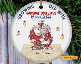 May include: A white round Christmas bauble featuring a cartoon illustration of an elderly couple dressed as Santa and Mrs. Claus entangled in Christmas lights. The text reads "Growing Old With Someone You Love Is Priceless". The names Kevin and Susan are printed below the couple.