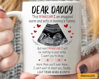 May include: White ceramic mug with the text "DEAR DADDY" and a message from a baby, including an ultrasound image and red heart accents. The mug is personalized with a yellow banner.