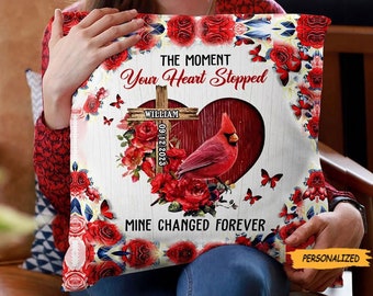 Peut inclure: Un cardinal rouge avec une croix en bois et des roses rouges sur un fond blanc. Le texte "The moment your heart stopped" et "Mine changed forever" est imprimé sur l'oreiller. La croix porte le nom "William" et la date "09.12.2023" imprimée dessus.