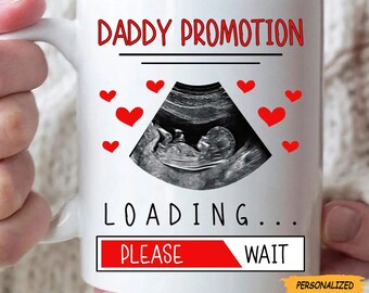 May include: White ceramic mug with the text "DADDY PROMOTION" in red, a sonogram image, and red heart graphics. Below the sonogram is the text "LOADING... PLEASE WAIT". The mug is personalized.