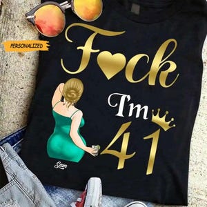 May include: Black t-shirt with gold text reading "F*ck I'm 41" with a heart symbol. A cartoon illustration of a woman in a green dress is on the left. The word "Personalized" is on a yellow tag.