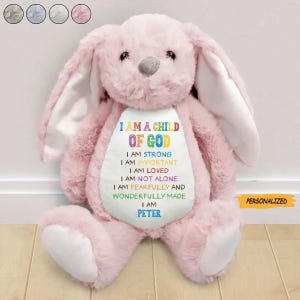 May include: A plush pink bunny with long ears and a gray nose. The bunny has a white belly with the text "I AM A CHILD OF GOD" and other affirmations. The name "PETER" is also on the bunny. The word "PERSONALIZED" is on a yellow tag.