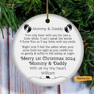 May include: A white ceramic Christmas ornament with the text "Mommy & Daddy" and a message about love and safety. The ornament includes the text "Merry 1st Christmas 2024" and the name "William". A gold string is attached for hanging.