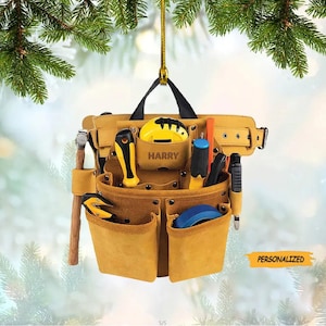 May include: A brown leather tool belt with multiple pockets and a personalized name tag that reads "HARRY". The belt is hanging from a tree branch and includes various tools, including a hammer, a tape measure, and a level.
