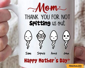 Peut inclure: Mug en céramique blanche avec les mots "Mom" et "THANK YOU FOR NOT Spitting us out" en texte rouge et noir. La tasse présente quatre illustrations de spermatozoïdes avec des noms en dessous. "Happy Mother's Day" est également imprimé sur la tasse.