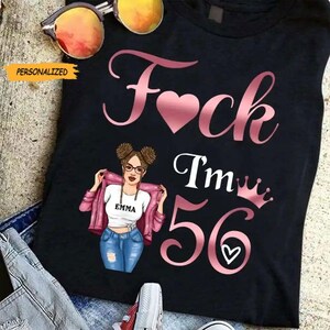 Peut inclure: T-shirt noir avec un motif rose disant "F*ck I'm 56" avec un cœur, une couronne et une illustration de femme. La femme porte des lunettes, un t-shirt blanc avec le nom "Emma", une veste rose et un jean bleu.