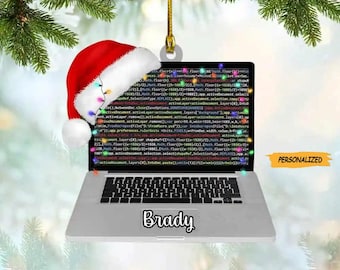 May include: A silver laptop computer ornament with a red Santa hat on top. The laptop screen displays code and the keyboard is visible. The ornament is personalized with the name "Brady".
