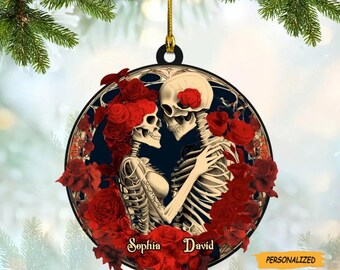 May include: Round Christmas ornament featuring a skeletal couple embracing, surrounded by red roses. The ornament has the names "Sophia" and "David" and the word "PERSONALIZED" printed on it. The background is a dark blue with a gold string for hanging.