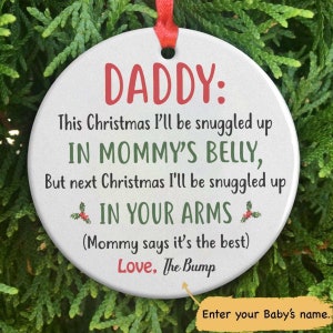 May include: White round Christmas ornament with red text that reads "DADDY: This Christmas I'll be snuggled up IN MOMMY'S BELLY, But next Christmas I'll be snuggled up IN YOUR ARMS (Mommy says it's the best) Love, The Bump".