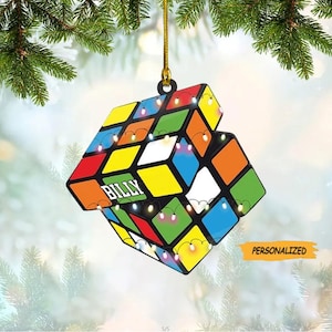 May include: A colorful, personalized Christmas ornament shaped like a Rubik's Cube with the name "Billy" on one side. The ornament has a string for hanging and features a design of a Rubik's Cube with lights.