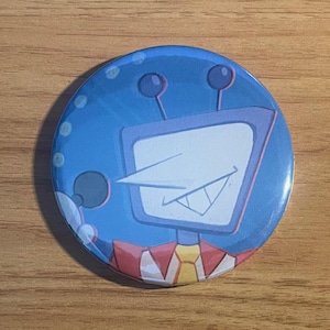 Puede incluir: Un botón redondo azul con la cara de un robot de dibujos animados con una pantalla blanca, una nariz larga y una sonrisa. El robot tiene dos antenas y un cuello rojo, amarillo y blanco. El fondo es azul con puntos blancos.