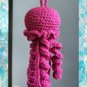 May include: A crocheted pink jellyfish with a long, curled tentacle hanging from the top.