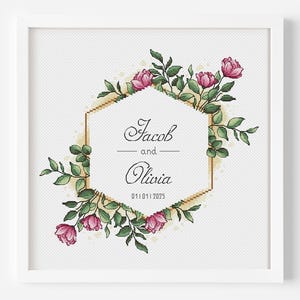Puede incluir: Un marco blanco con un marco hexagonal dorado con el texto "Jacob y Olivia 01.01.2023" rodeado de flores rosas y hojas verdes.