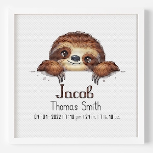 Könnte beinhalten: Ein gerahmtes Kreuzstichbild mit einem braunen Faultier, das über eine weiße Oberfläche blickt. Der Text lautet "Jacob Thomas Smith" mit Geburtsdaten.