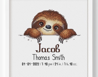 May include: A framed cross-stitch featuring a brown sloth peeking over a white surface. The text reads "Jacob Thomas Smith" with birth details: 01-01-2022, 7:10 pm, 21 in., 1 lb. 10 oz.