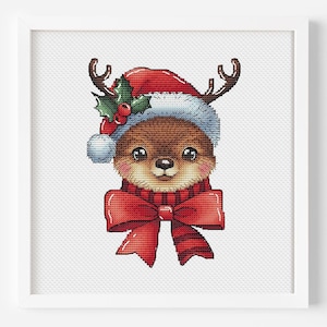 Puede incluir: Un ciervo marrón y blanco con cuernos que lleva un gorro de Papá Noel rojo con una rama de acebo verde y una pajarita roja.