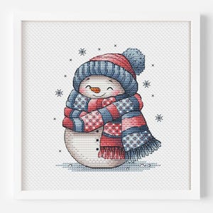 May include: A framed cross-stitch of a smiling snowman wearing a blue and red hat and scarf. The snowman has a carrot nose and black button eyes. Snowflakes are scattered around the snowman.