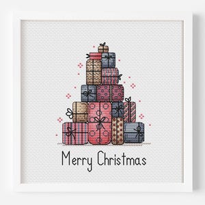 May include: A framed cross-stitch artwork featuring a stack of colorful gift boxes arranged in a Christmas tree shape. The boxes are in shades of pink, blue, brown, and gold, with black bows and accents. The words "Merry Christmas" are stitched below.