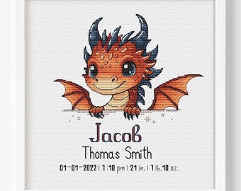 May include: A framed cross-stitch featuring a cartoon dragon with orange and blue scales. The dragon is peeking over a ledge with the name "Jacob" and other details below. The frame is white.
