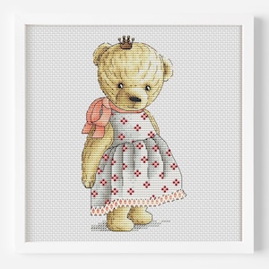 Puede incluir: Un patrón de punto de cruz de un oso de peluche con una corona y un vestido rosa y blanco con lunares rojos.
