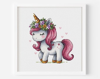 Puede incluir: Un punto de cruz enmarcado de un unicornio de dibujos animados. El unicornio tiene un cuerpo blanco, melena y cola rosas, y un cuerno dorado. Lleva una corona floral con flores moradas, amarillas y verdes. El fondo es blanco.
