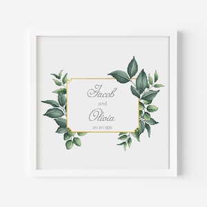 Peut inclure: Une impression encadrée blanche avec un cadre doré et un feuillage vert entourant un rectangle blanc avec le texte "Jacob et Olivia 01.01.2024" en écriture cursive noire.