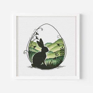 Może przedstawiać: Czarna sylwetka królika siedzącego w zielono-białym wzorze w kształcie jajka. Jajko otoczone jest zieloną roślinnością i wzgórzami.