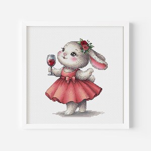 Puede incluir: Un conejito blanco con un vestido rojo con un lazo y una corona de flores sostiene una copa de vino tinto.