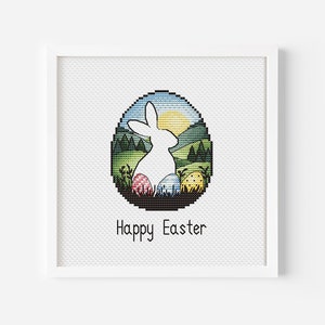 Puede incluir: Patrón de punto de cruz con una silueta de conejo blanco dentro de un marco en forma de huevo. El fondo es un paisaje colorido con un sol y colinas verdes. El texto "Feliz Pascua" está debajo del huevo.