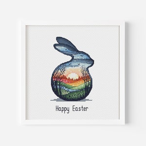 May include: A framed cross-stitch artwork featuring a blue bunny silhouette with a landscape scene inside. The scene includes a sunset, trees, and a river. The words "Happy Easter" are stitched below the bunny.