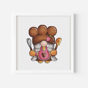May include: A cross-stitch pattern featuring a gnome wearing a brown chef's hat with a strawberry on top, a pink apron with a heart, and holding a whisk and a spatula.