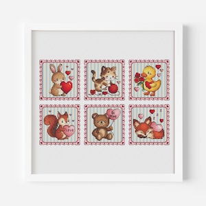 Op de afbeelding: Een ingelijst kunstwerk met zes kruissteekvierkanten met Valentijnsdagthema's. Elk vierkant toont een ander dier dat een hart of ballon vasthoudt. De dieren zijn een konijn, kat, eend, eekhoorn, beer en vos, tegen een lichte achtergrond.