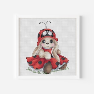 Può includere: Uno schema di punto croce di un coniglio carino che indossa un costume da coccinella. Il coniglio è seduto su un pezzo di erba verde e ha un vestito rosso con pois neri.