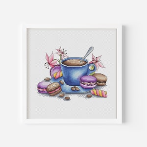 Op de afbeelding: Een blauwe koffiekop met een lepel, gevuld met koffie, omringd door roze bloemen en macarons.