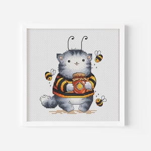 Può includere: Un gatto grigio che indossa un maglione a strisce gialle e nere con un barattolo di miele nelle zampe. Il gatto ha due antenne ed è circondato da api.