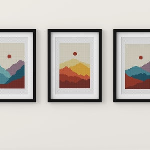 May include: Three framed prints of pixelated mountain landscapes with a red sun in the sky. The mountains are different colours in each print: blue, purple, and red; orange, yellow, and red; and blue, purple, and red.