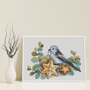 May include: A blue bird with a yellow star in its beak sits on a bed of green and brown leaves and yellow star-shaped ornaments.