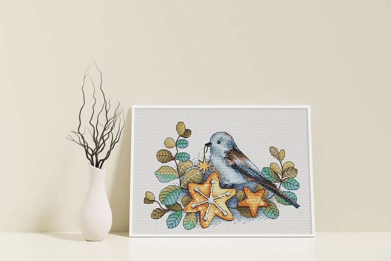May include: A blue bird with a yellow star in its beak sits on a bed of green and brown leaves and yellow star-shaped ornaments.