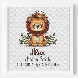 May include: A framed cross-stitch featuring a cartoon lion wearing a crown, surrounded by green leaves. The lion is brown and tan with a friendly expression. Below the image are the words "Alex Jordan Smith" and birth details: 21 inches, 1 lb 10 oz.