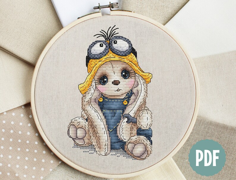 K&ouml;nnte beinhalten: Kreuzstichmuster eines niedlichen Kaninchens, das ein gelbes und schwarzes Minion-Kost&uuml;m mit Schutzbrille tr&auml;gt. Das Kaninchen sitzt mit gekreuzten Pfoten und hat einen s&uuml;&szlig;en Gesichtsausdruck.