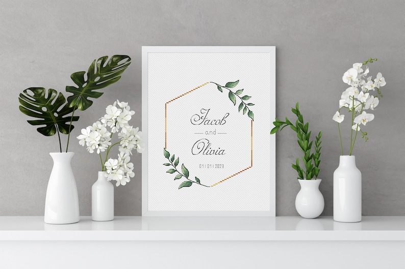 May include: A white framed print with a gold geometric frame and green foliage. The text on the print reads "Jacob and Olivia 01.01.2023".