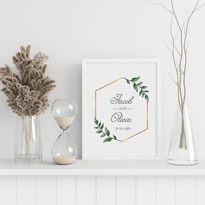 May include: A white frame with a gold hexagon and green leaves surrounding the text "Jacob and Olivia 01.10.1.2023".