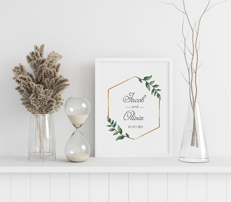 May include: A white frame with a gold hexagon and green leaves surrounding the text "Jacob and Olivia 01.10.1.2023".